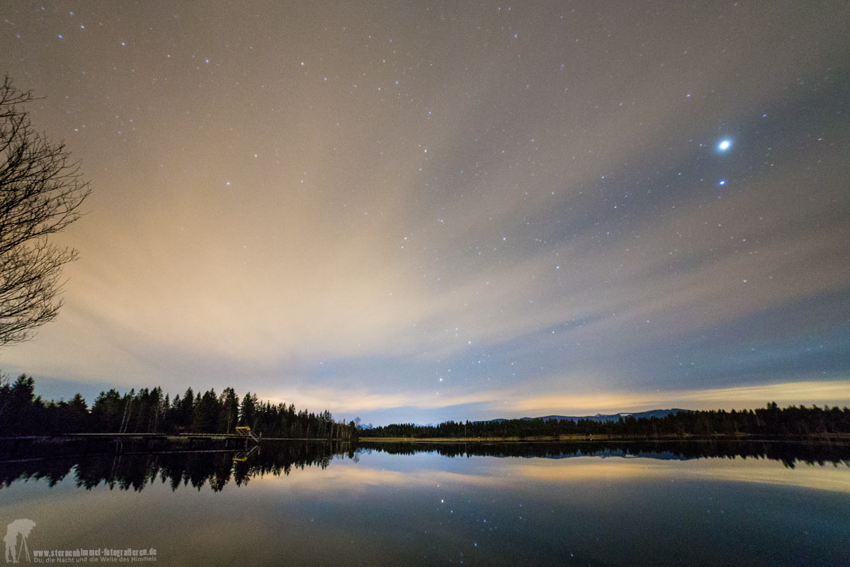 Cirruswolken am Nachthimmel mit Sternen über einem See in Bayern